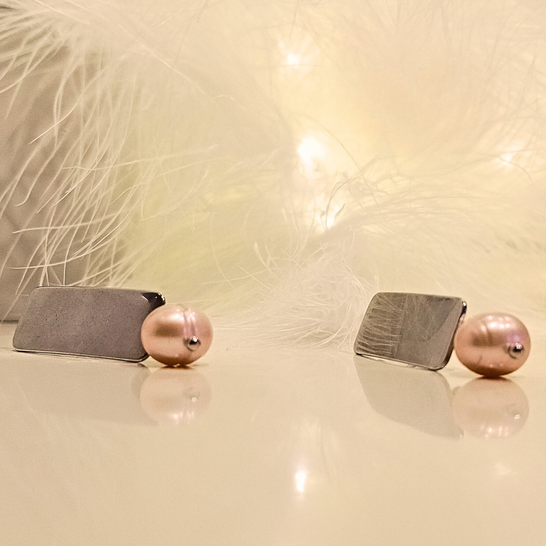 Polished Stainless Steel Örhängen med rosa sötvattenspärlor mot vit fjäderbakgrund och varmt ljus
