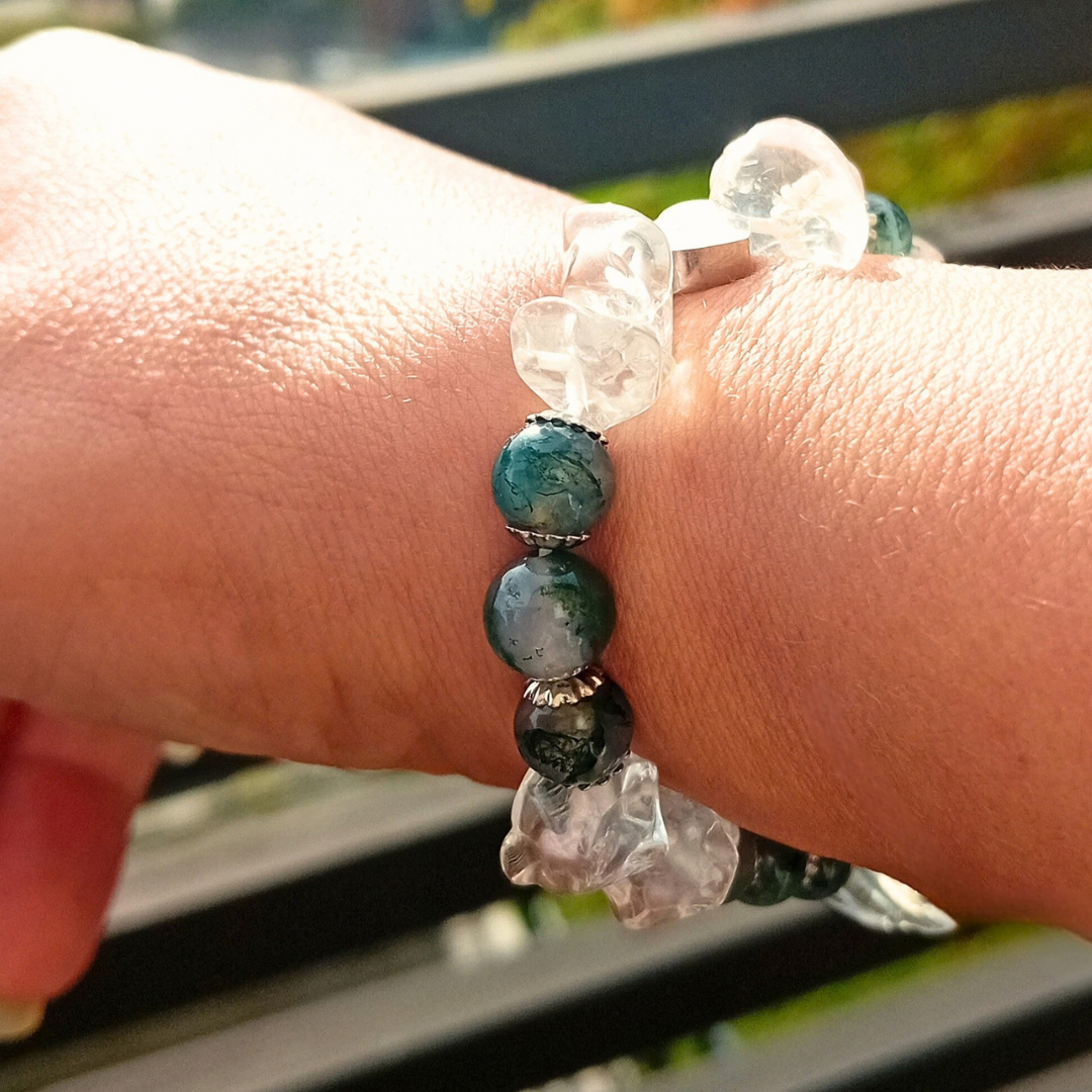 Närbild på FAELYN-armband på handleden i solljus, mörkgröna mossagatpärlor mellan klara, huggna bergkristaller