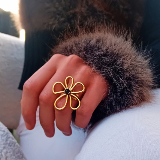 IRIS-ring på handen, guldfärgad blomma med en mörk tigerögecabochon i mitten, handen vilar mot en fuskpälskrage i solnedgång