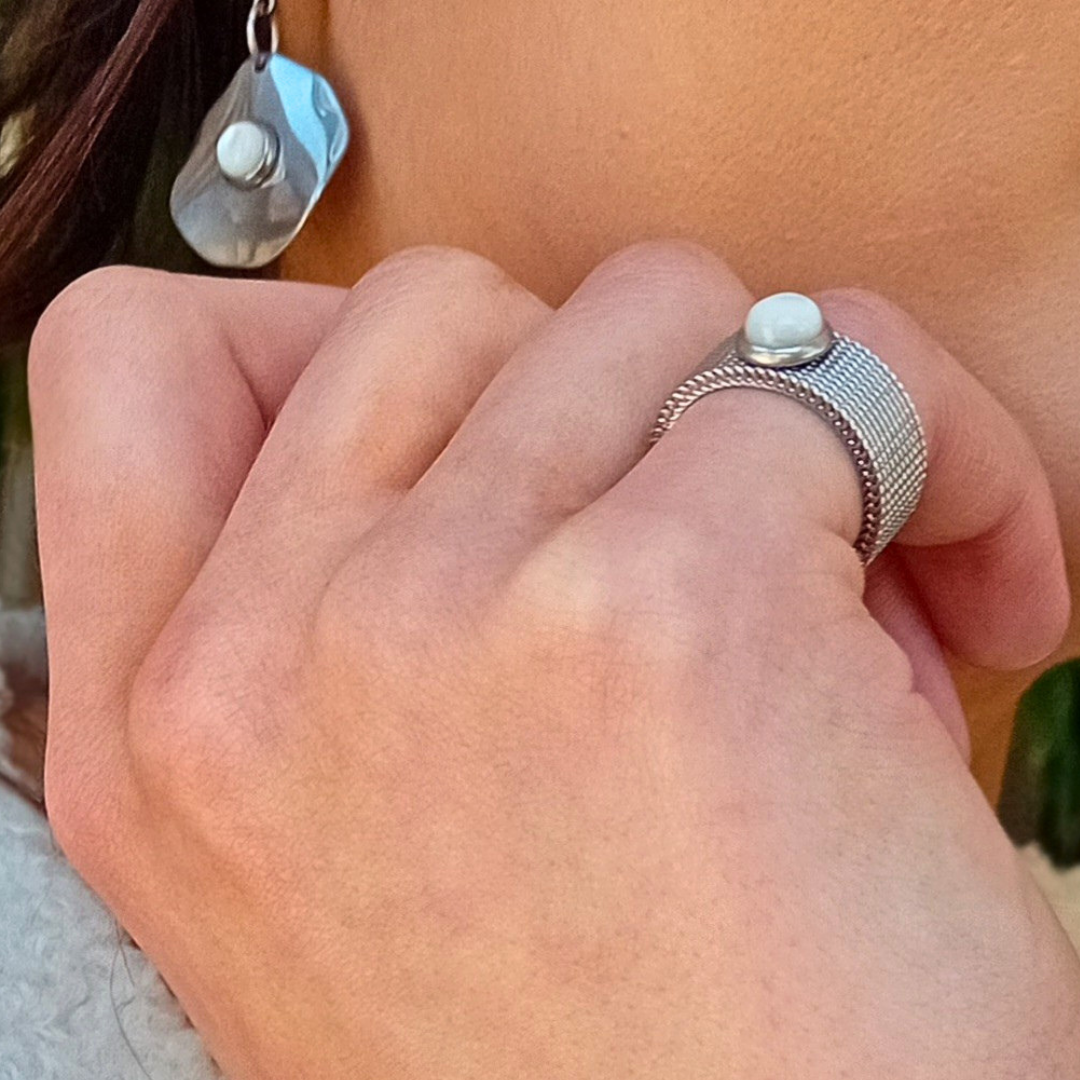 LUNË mesh ring in stainless steel with mother of pearl cabochon worn on finger in natural light, showing soft luminous reflection and clean modern design.