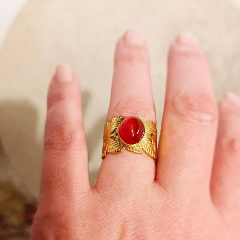 MEROPE-ring på fingret med oval karneolcabochon i guldfärgad infattning, omgiven av graverade bladformer