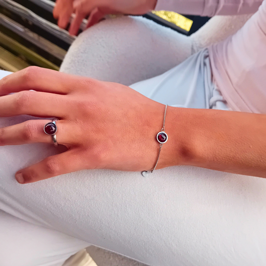 VITIA-ring och VITIA-armband på handen, båda med rund, vinröd granatcabochon i högpolerat rostfritt stål