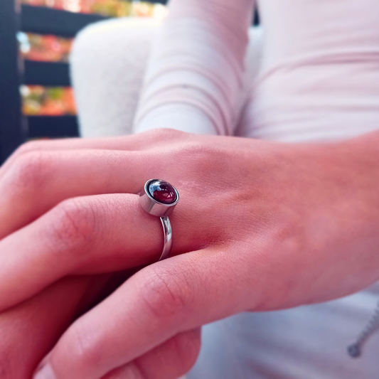 Närbild på VITIA-ring på handen, med en oval granatcabochon i högpolerad infattning  som döljer ringens justerbara öppning
