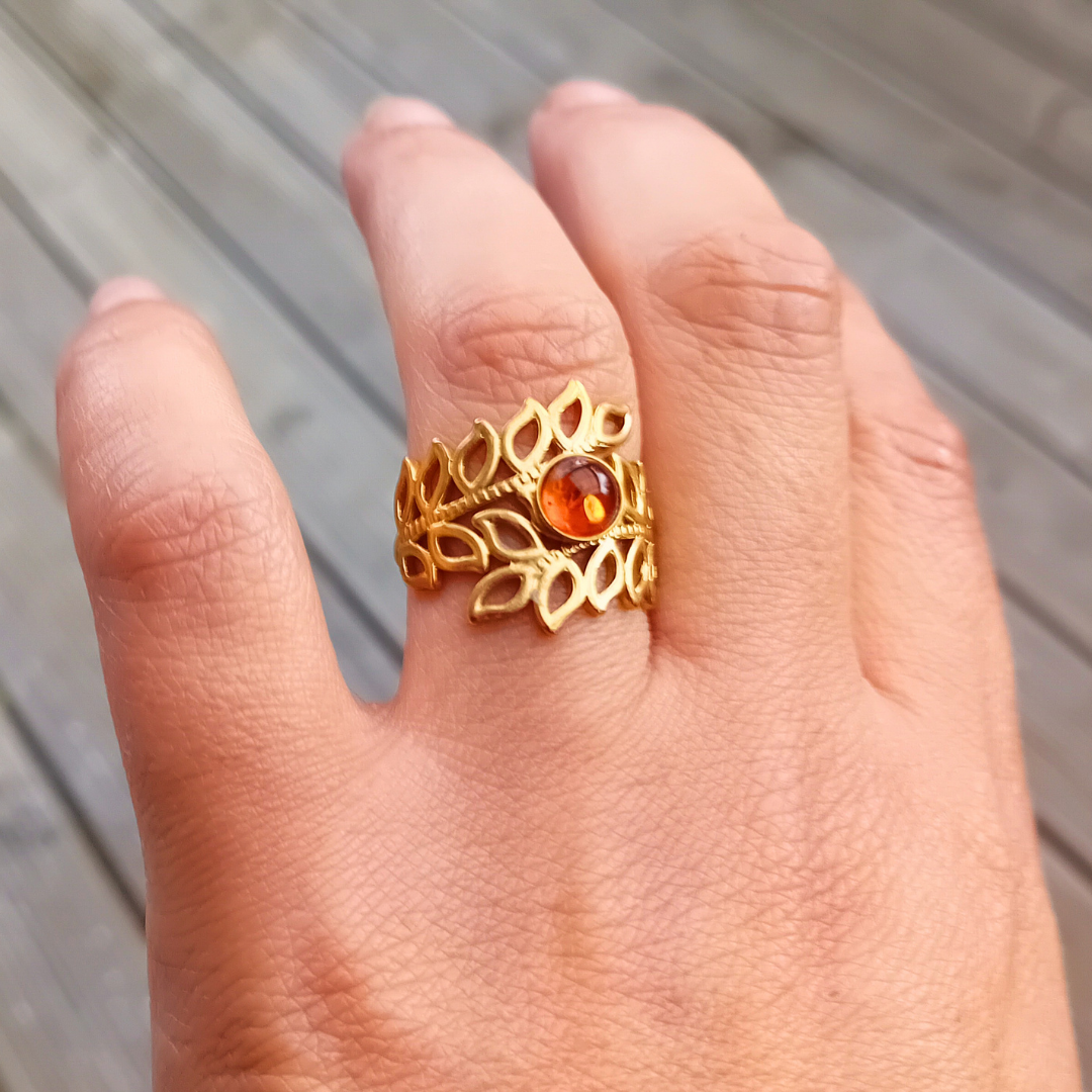 ARDEN-ring på fingret med cognacfärgad bärnstenscabochon omgiven av en krans av öppna, guldskimrande blad