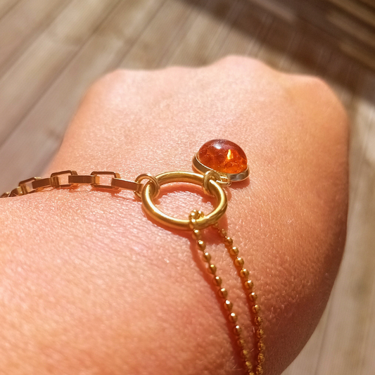 ENID-armband på handleden med kedja av rektangulära guldlänkar, en öppen guldcirkel och en cognac färgad bärnstenscabochon i infattning