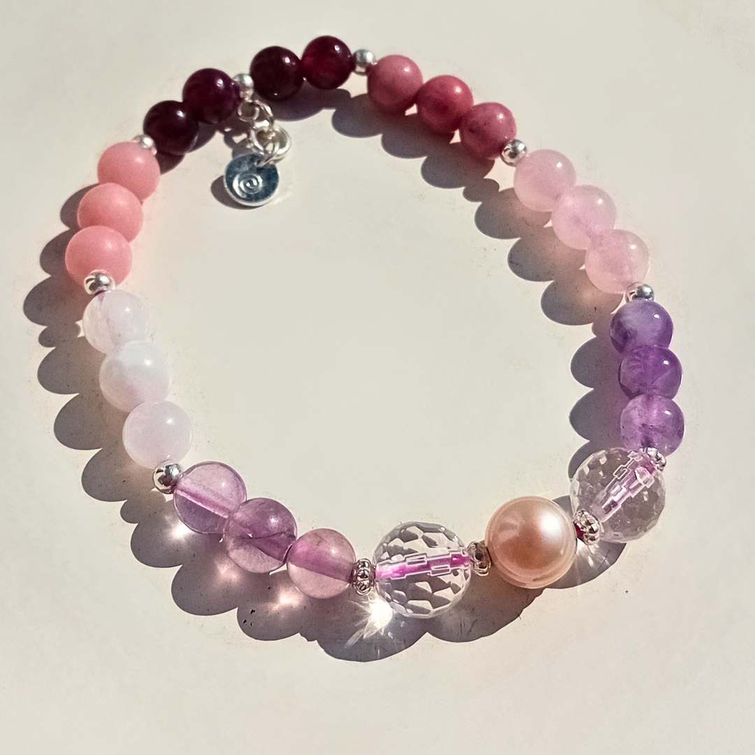 Ennea armband med rosa, lila och vinröda ädelstenspärlor, fasetterade kristaller och äkta sötvattenspärla i 925 sterling silver, mot ljus bakgrund.
