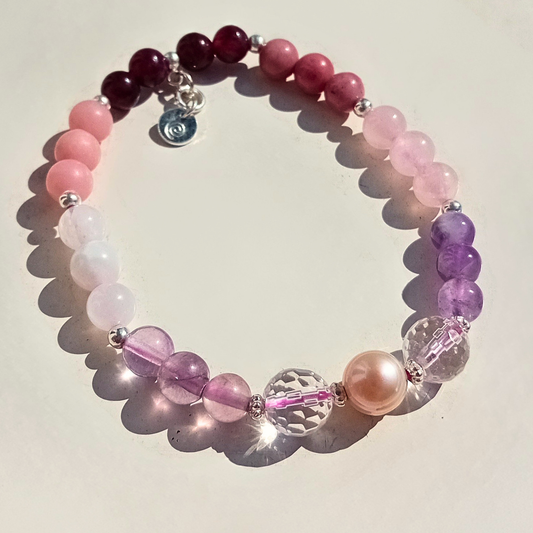 Ennea armband med rosa, lila och vinröda ädelstenspärlor, fasetterade kristaller och äkta sötvattenspärla i 925 sterling silver, mot ljus bakgrund.