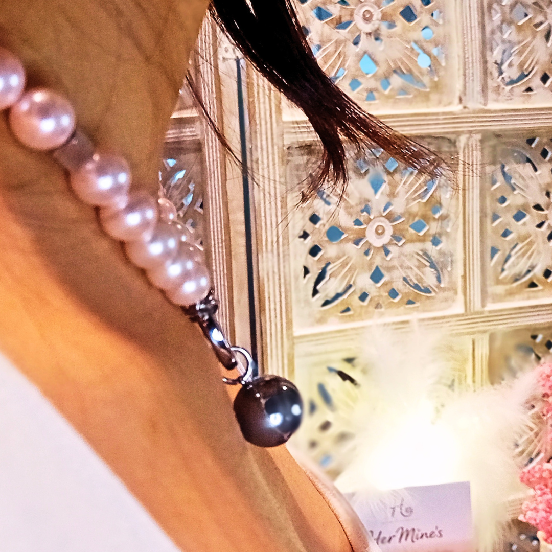 Närbild av choker i rostfritt stål med 10 mm shell pearls i roséton och frontlås med hängande droppdetalj