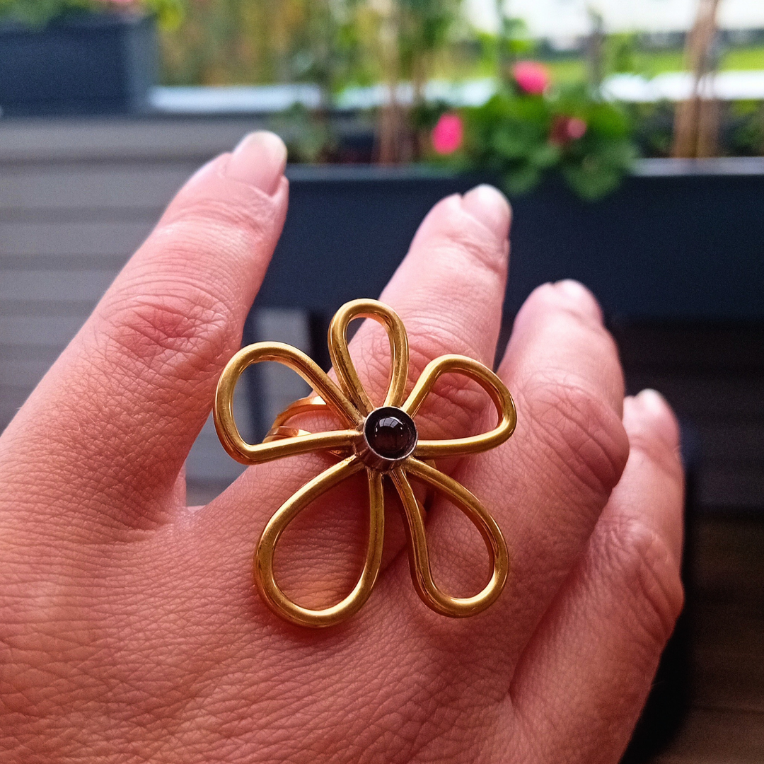 IRIS-ring på handen med en blomma av fem öppna, guldfärgade kronblad och en liten mörk tigerögecabochon i silverfärgad infattning i mitten