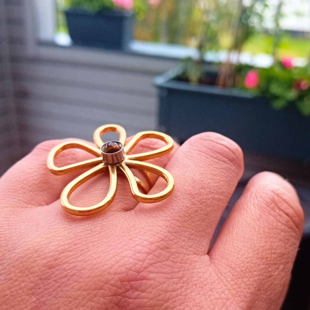 IRIS-ring sedd snett från sidan på handen, med en blomma av fem öppna, guldfärgade kronblad och en liten brun tigerögecabochon i silverfärgad infattning