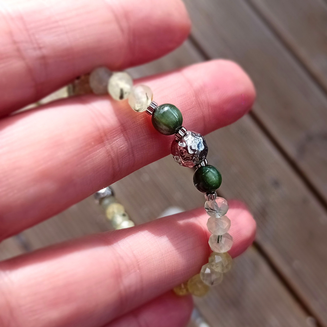 Armbandet LIVIA i prehnit och serafinit med hamrat rostfritt stål, hållet i handen i solljus mot en träbakgrund.
