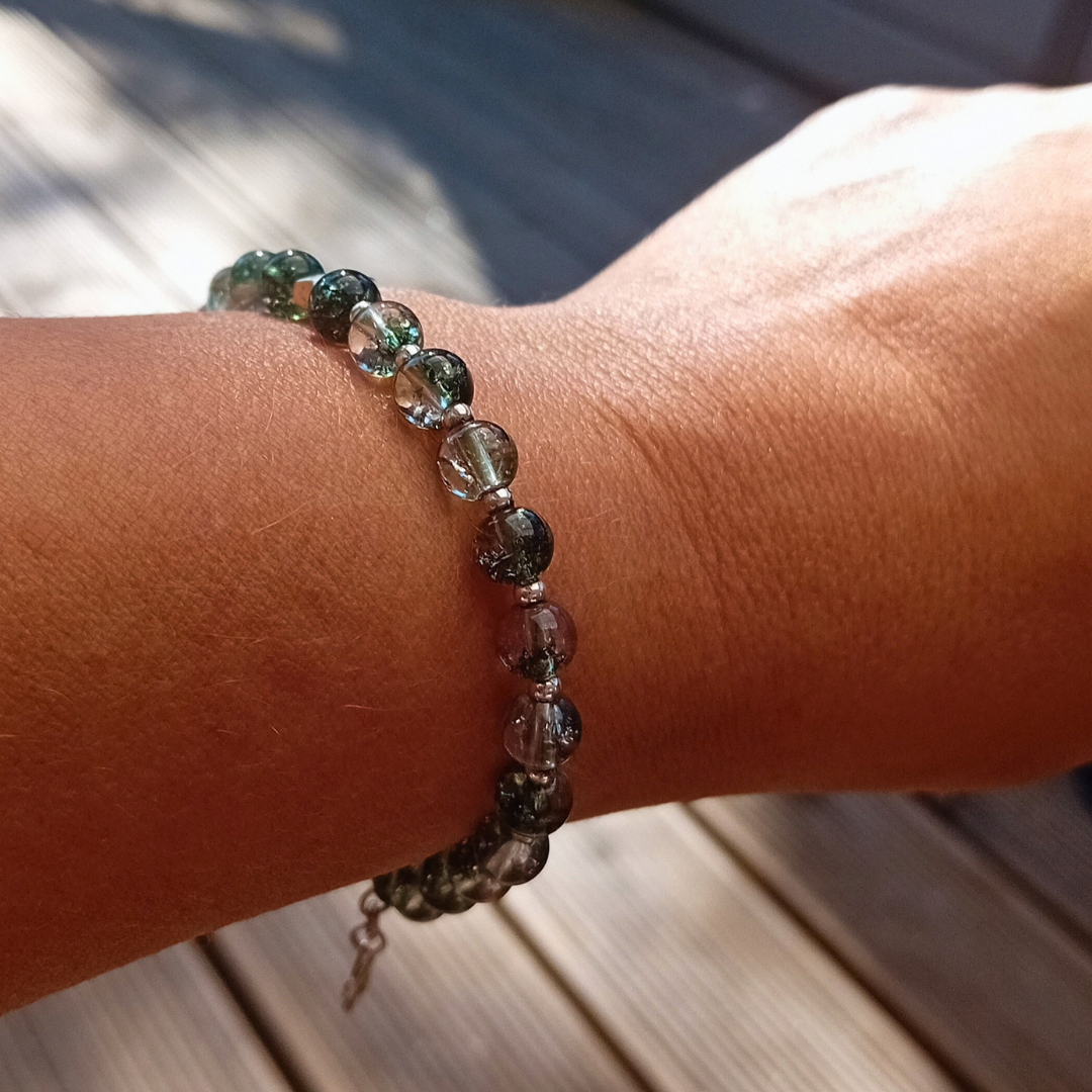 MIRA-armband på handleden i solljus, gröna och klara fantomkvartspärlor som glittrar