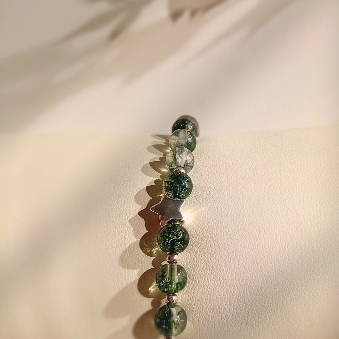 Närbild på MIRA-armband med gröna fantomkvartspärlor och en liten silverstjärna, mjukt skuggspel i bakgrunden