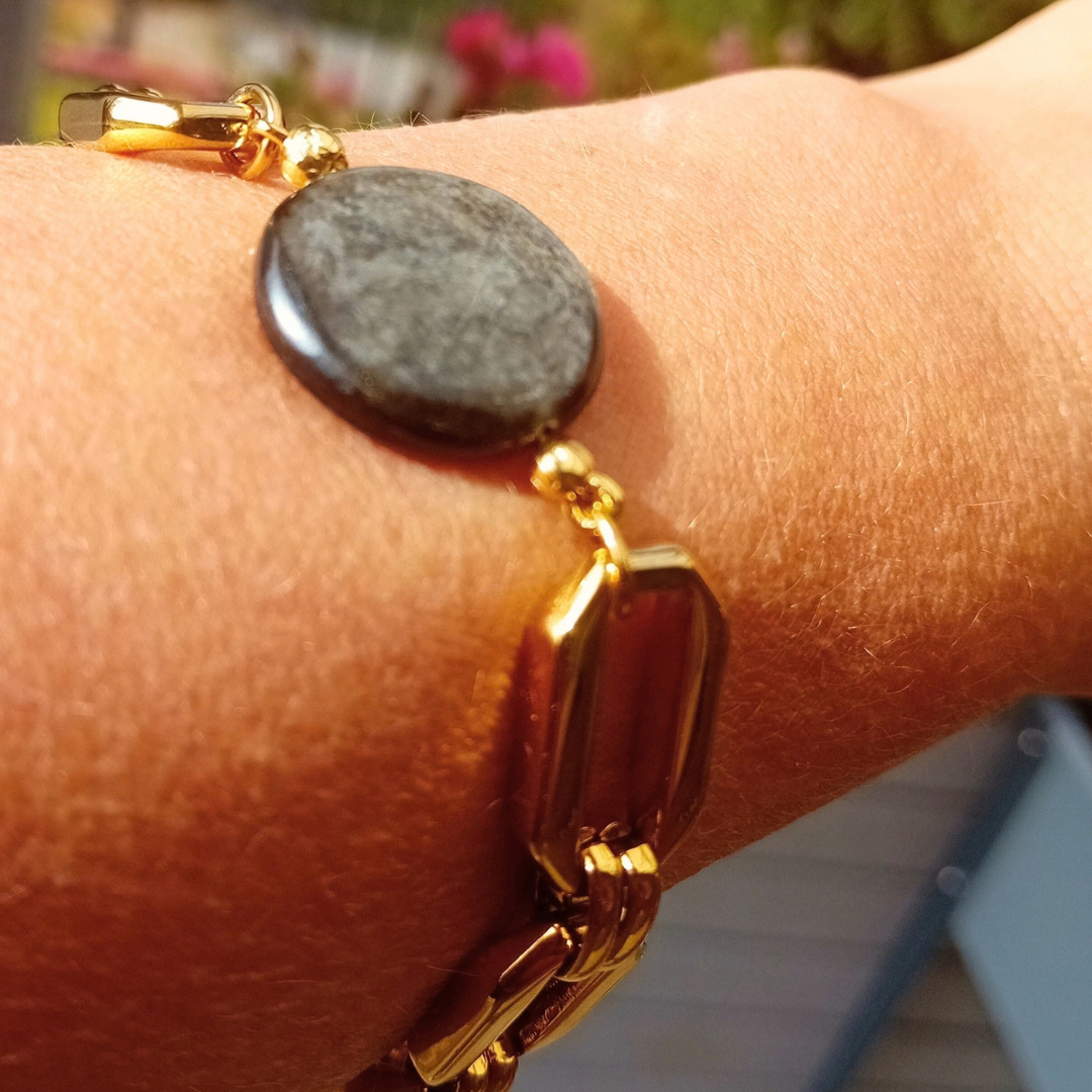 Armbandet Raven med golden mica-coin och guldpläterad länk, buret på handleden i solljus.