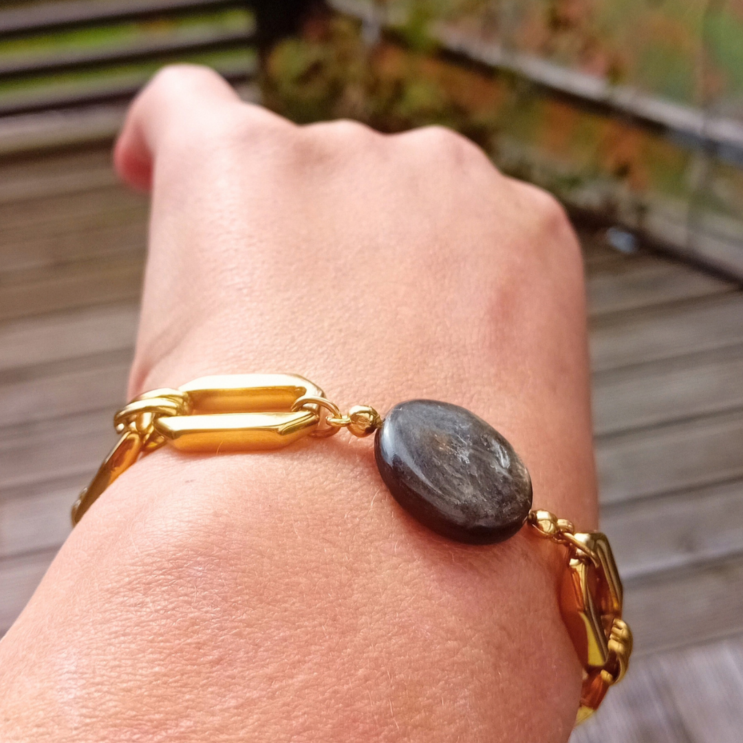 Närbild på Ravens golden mica-coin i profil mot guldpläterad länk, buret på handryggen i höstens dagsljus.